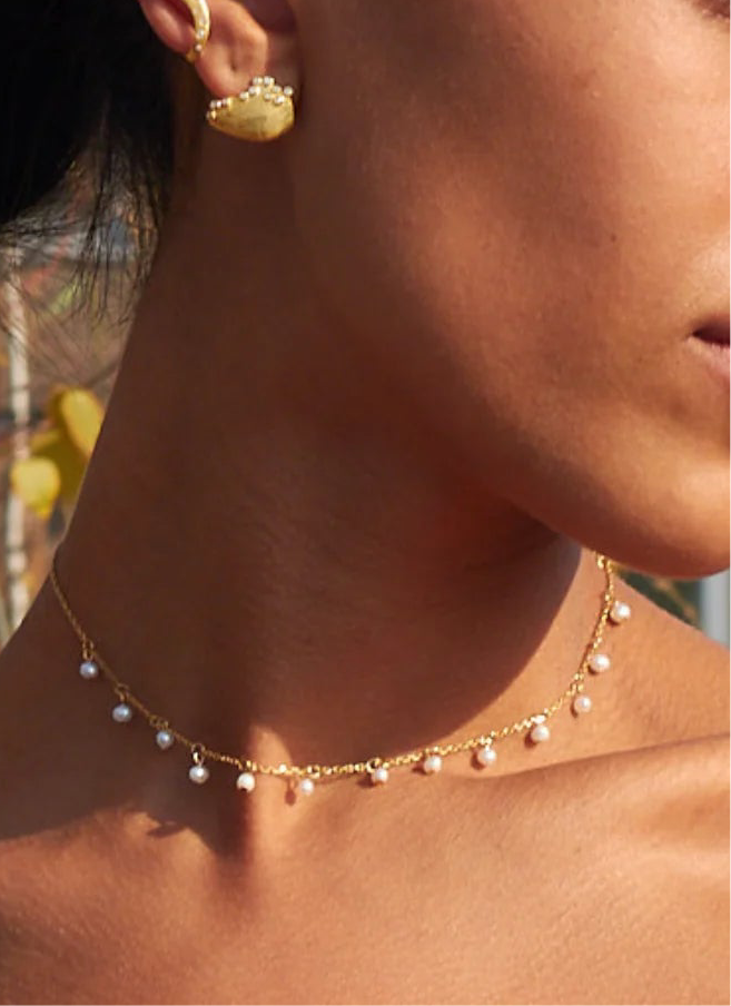 Close-up of a model wearing the Pearl Droplets Adjustable Choker, featuring small white pearl drops spaced along a fine gold-tone chain at the collarbone.