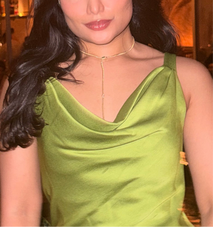 Photo of model wearing transformable necklace in yellow gold finish in a lariat shape, styled with parrot green cowl neck. The necklace lariat is dropping into the cowl of the dress 