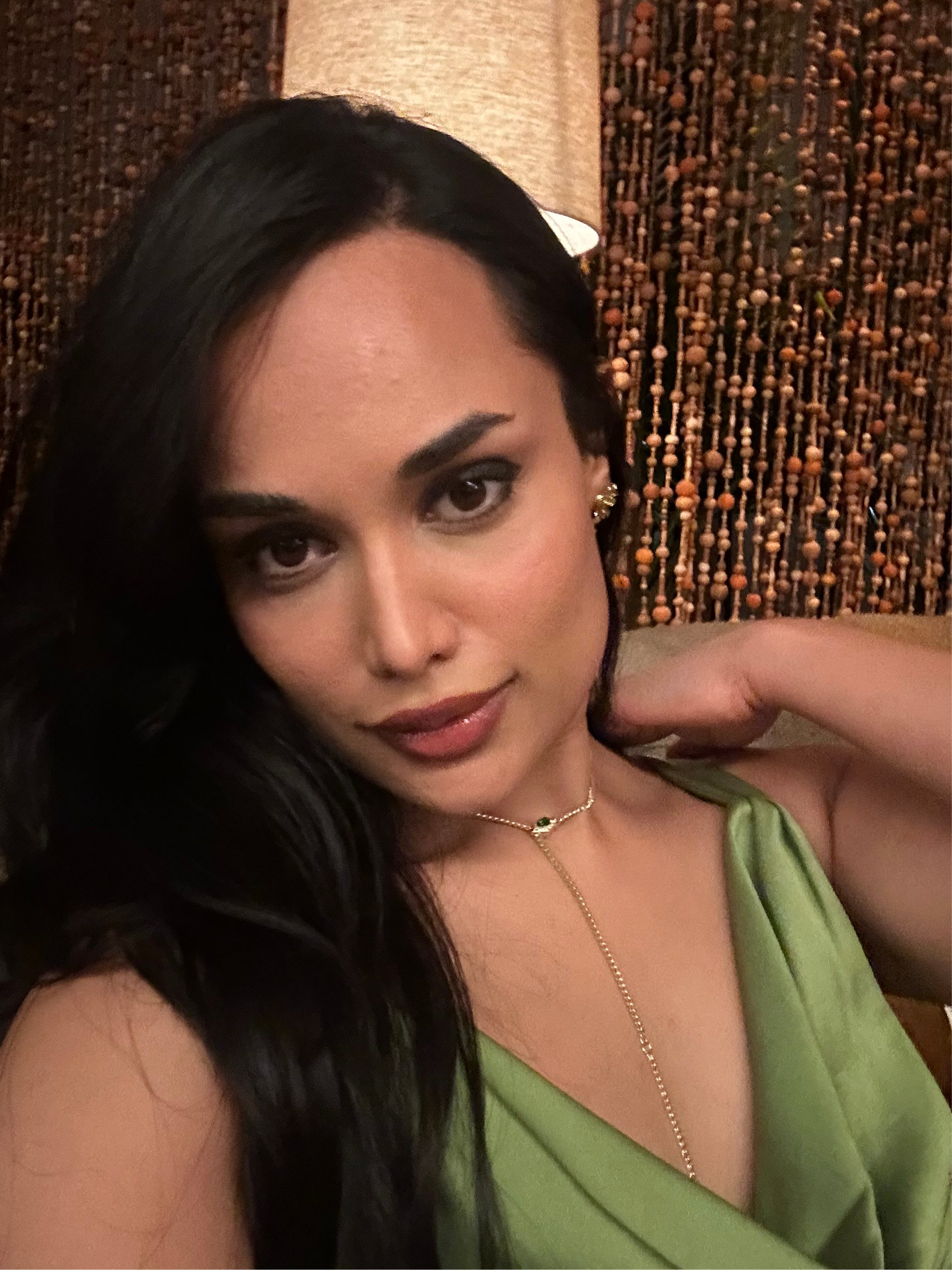 Photo of model wearing transformable necklace in yellow gold finish in a lariat shape, styled with parrot green cowl neck. 