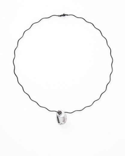 Contemporary necklace featuring a sculptural silver-tone pendant on a wavy black gold vermeil chain, styled against a white background