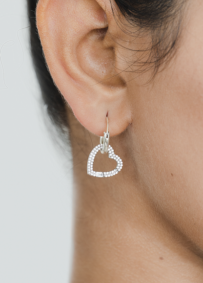 Close-up view of a single silver heart earring encrusted with stones, dangling from a small hoop. The design is delicate and stylish, adding a hint of sparkle to the ear.