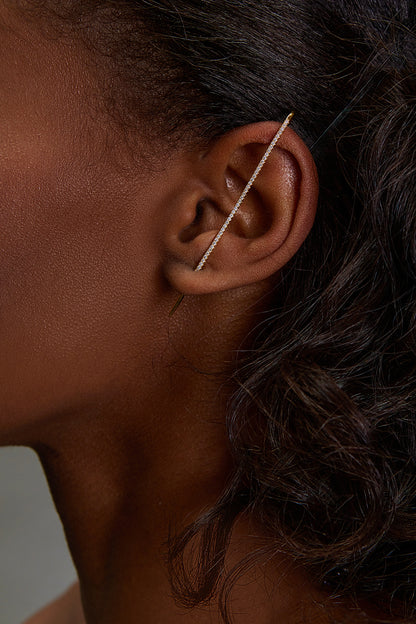 Close-up image of a model wearing the Tacenda Ear Pin, a slim, sparkling earring designed to hook onto the top of the ear, requiring only one lobe piercing. It stands out as a statement piece, showcasing a blend of elegance and modern edge against the model's ea