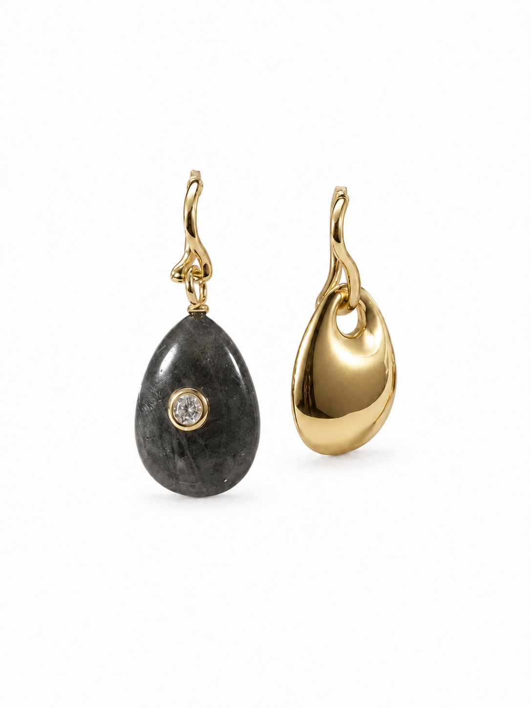 Mismatched yellow-gold wavy hoop earrings with removable charms: one full-width dark natural-stone teardrop with a clear bezel-set stone and one polished sculptural gold teardrop, on white.