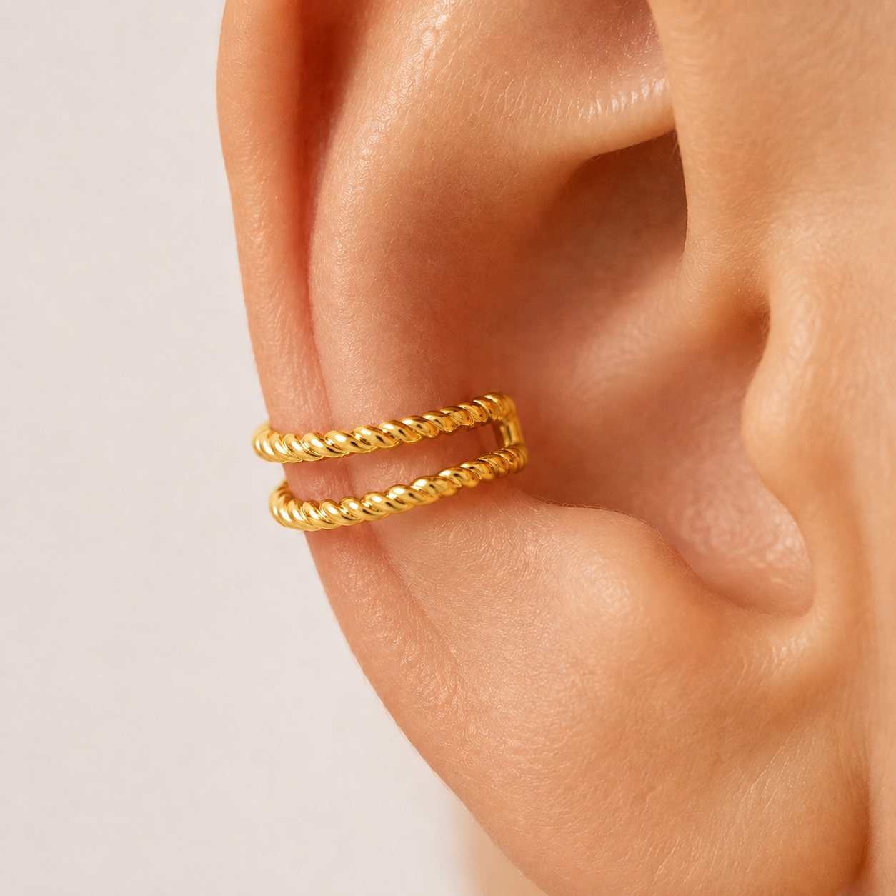 Yellow gold double rope ear cuff worn on ear, close-up