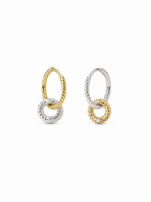 Mismatched pair of two-tone interlocking loop earrings, with one yellow-gold twisted huggie and white-gold drop loop and one white-gold huggie with yellow-gold drop loop, on white.