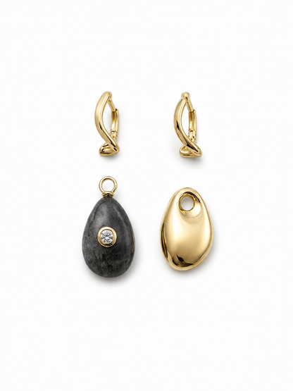 Two identical yellow-gold wavy hinged hoops displayed separately from their removable mismatched charms: one dark natural-stone teardrop with a clear bezel-set stone and one polished gold teardrop.