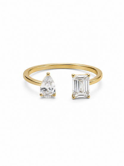 Yellow gold adjustable bypass ring with a clear pear-cut stone and emerald-cut stone on a white background.