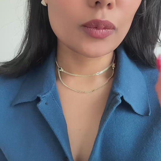 Video of person saying “wait for it” and showing the numerous ways this necklace featuring emerald green accents and dainty Cuban chain can transform. She is wearing the necklace in yellow gold finish and styled with a bright blue shirt 