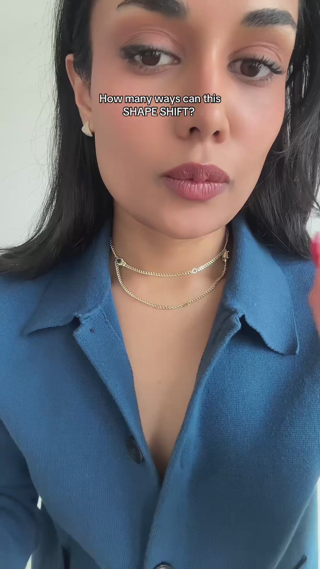 Video of person saying “wait for it” and showing the numerous ways this necklace featuring emerald green accents and dainty Cuban chain can transform. She is wearing the necklace in yellow gold finish and styled with a bright blue shirt 