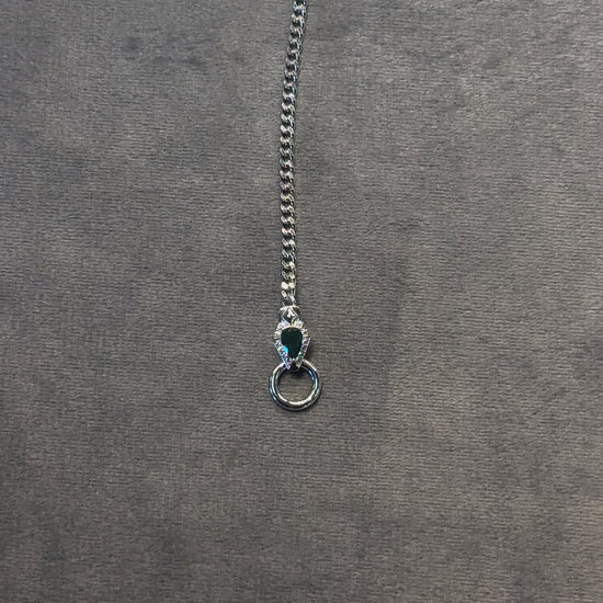 video of convertible/modular necklace featuring emerald green accent and dainty curb chain in platinum/ white gold finish, displayed in a lariat shape on a grey background. The video moves from bottom to the top to show details of the jewelry.