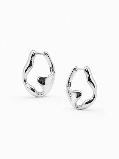 Mirrored pair of sculptural white-gold wave hoop earrings, with the left earring higher and the right earring slightly lower on a white background.
