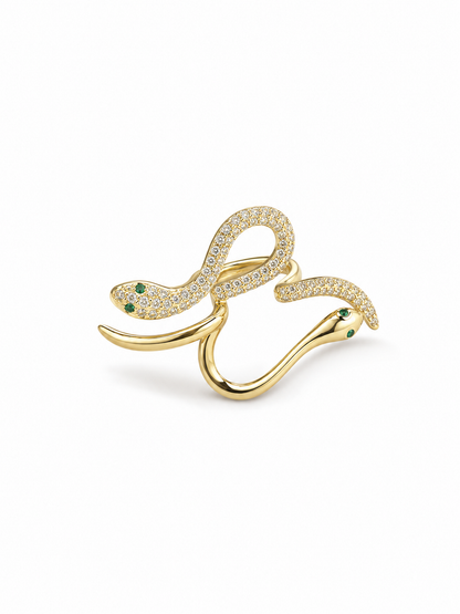 Adjustable double-serpent wrap ring in yellow gold with one clear pavé serpent, one polished serpent and small green eye details on white.